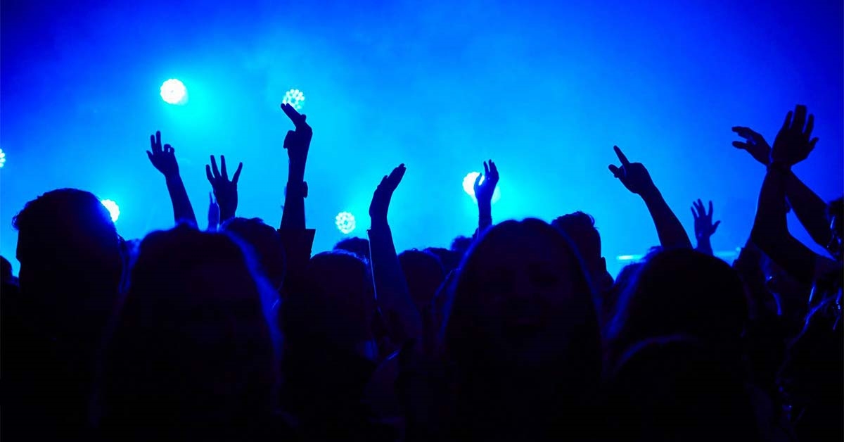 A photo of people with their hands up at a late-night event, with blue lighting and smoke effects
