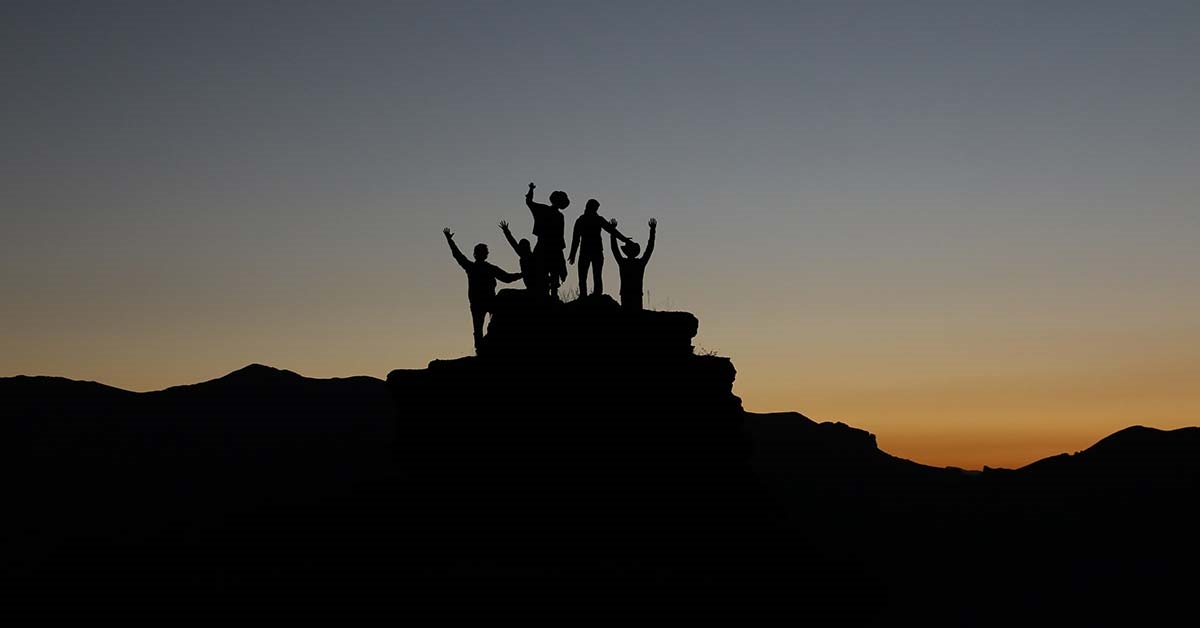 A group of people stood on a hill silhouetted by the sunset