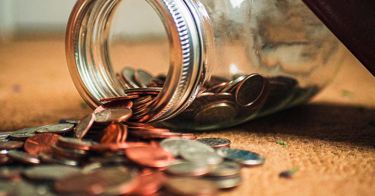 A jar lying on its side on a table with coins spilling out