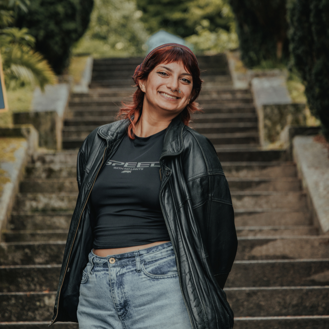 Image shows Aisha smiling at the camera stood on some steps, she is wearing a leather jacket