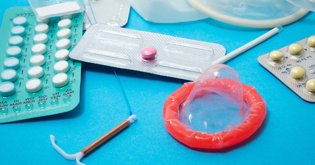 A condom, a coil implant and packets of contraceptives on a table